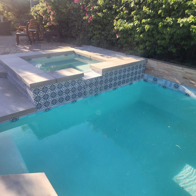 Completed remodel with patterned blue and white tile and new coping